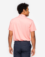 Orange pink coral golf performance polo with navy blue collar detail and two button placket paired with dark grey shorts