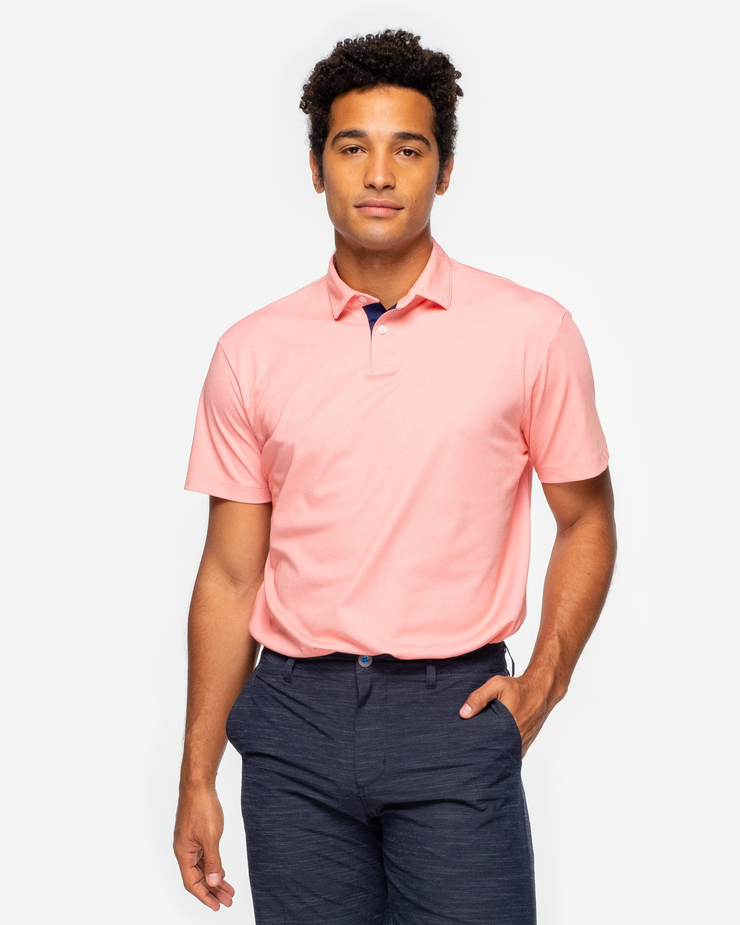 Orange pink coral golf performance polo with navy blue collar detail and two button placket paired with dark grey shorts