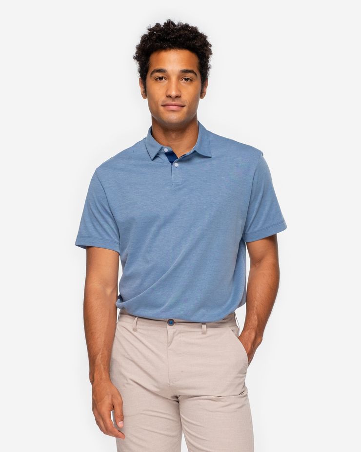 Heathered light blue golf performance polo with navy blue collar detail and two white button placket paired with khaki shorts