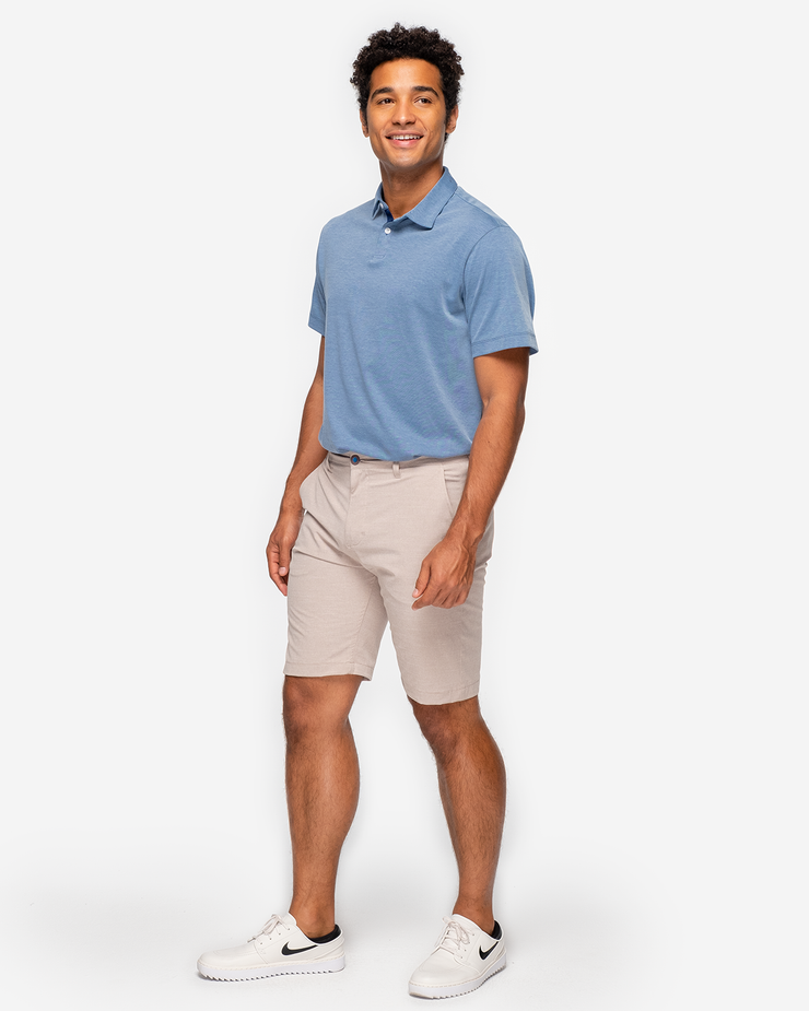 Heathered light blue golf performance polo with navy blue collar detail and two white button placket with khaki shorts