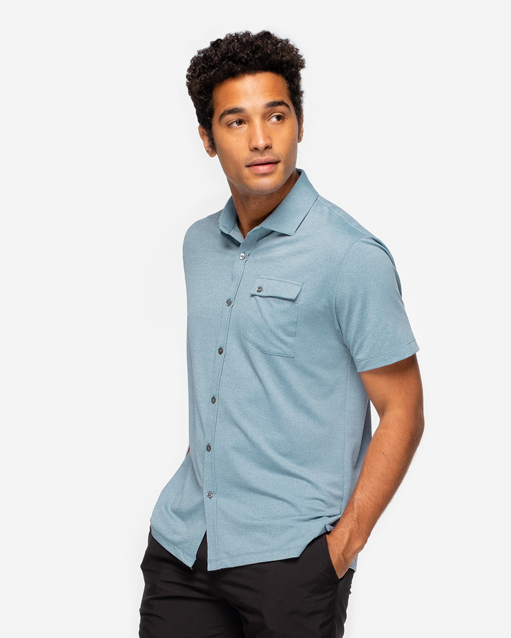 Blue-green textured short sleeve button down with asymmetric left chest pocket with button paired with black shorts