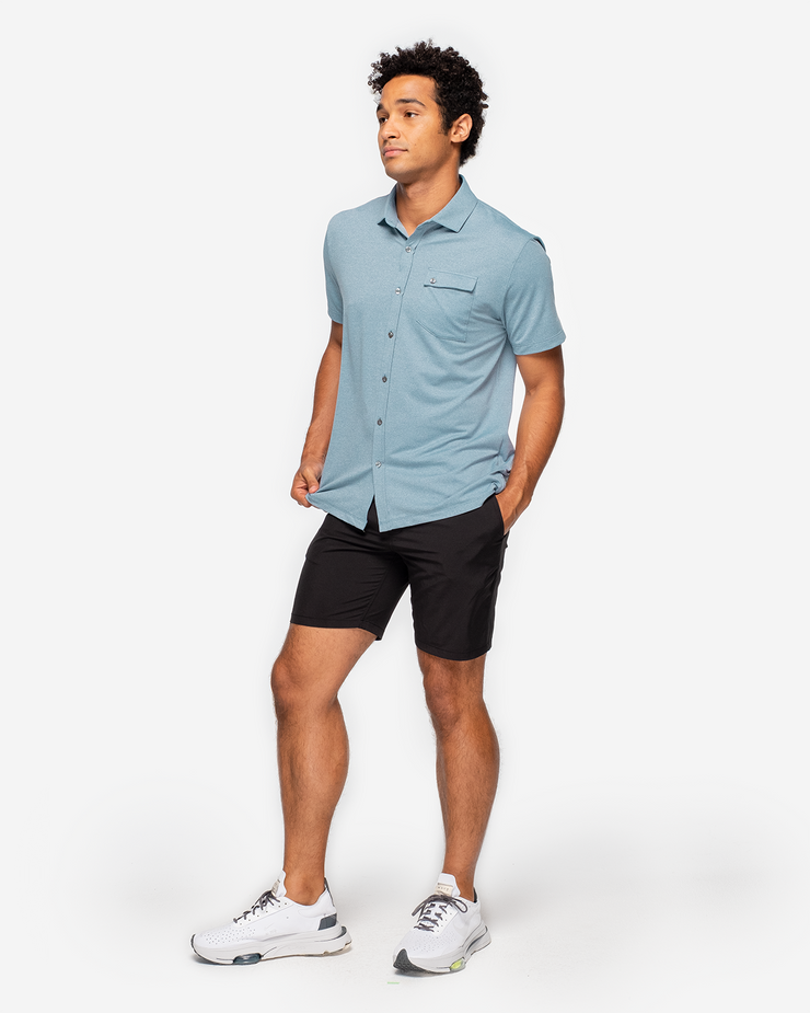 Blue-green textured short sleeve button down with asymmetric left chest pocket with button paired with black shorts